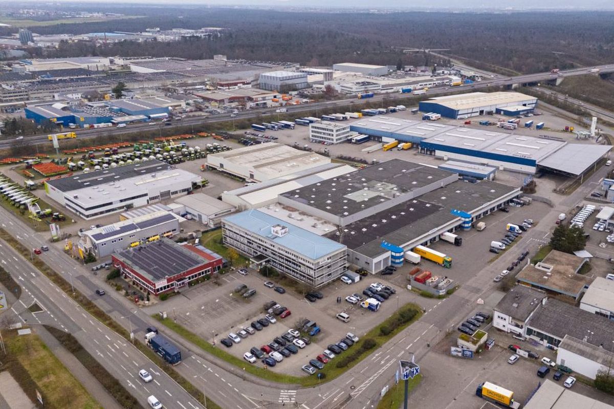 Luftaufnahme eines Industriegebiets mit Lagerhallen, Parkplätzen und LKWs in der Nähe einer Hauptstraße.