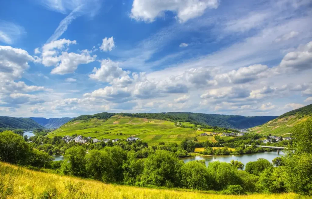 Grüne Hügel, Weinberge, ein gewundener Fluss und verstreute Dörfer unter einem teilweise bewölkten blauen Himmel.